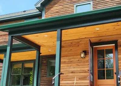 Green seamless gutters on a cedar-sided Vermont home with a covered porch