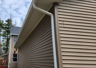 Tan vinyl-sided Vermont home with white seamless gutters and a downspout at the gable end