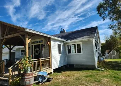 White farmhouse in Addison County VT with a timber-frame porch and seamless gutters